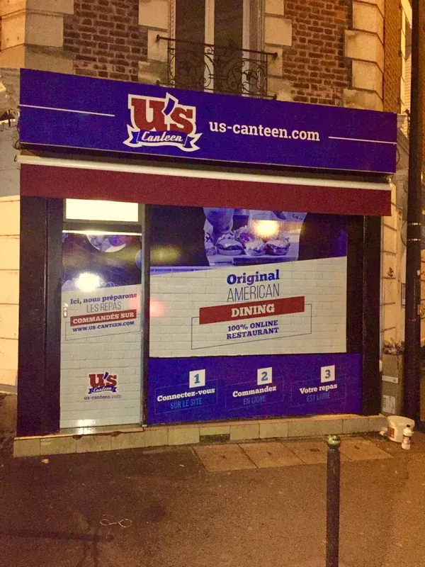 Devanture d'un restaurant U's Canteen la nuit, enseigne bleue et vitrine « Original American Dining ».
