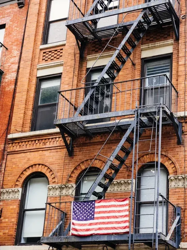 Façade de briques new-yorkaise, escalier de secours et drapeau américain à une fenêtre.