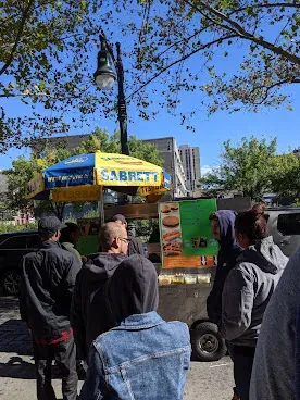 Petite foule attendant devant un kiosque à hot-dogs, sur un trottoir new-yorkais.