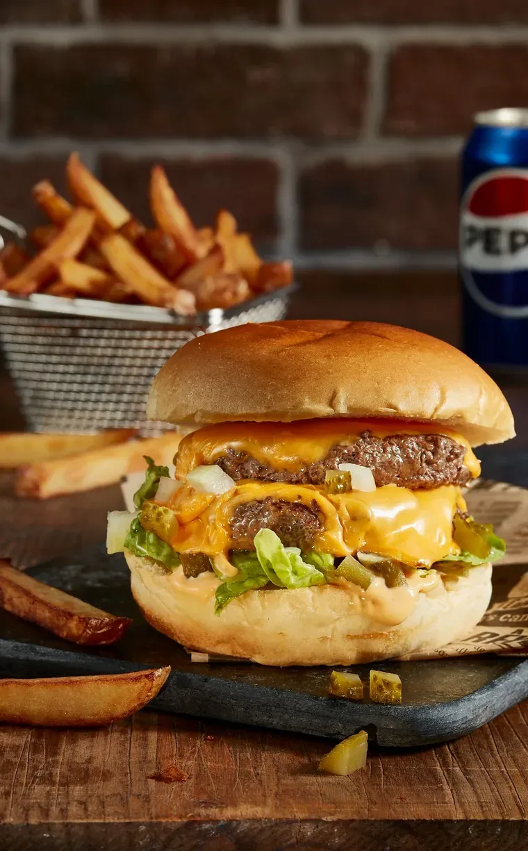 Burger double au cheddar fondu, cornichons et oignons, servi avec des frites