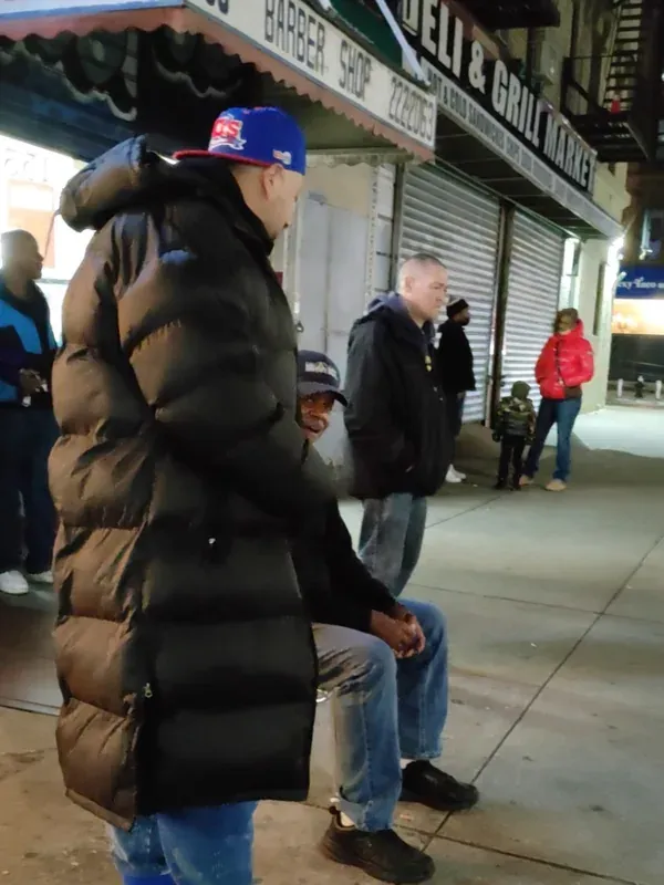 Hommes discutant sur un trottoir de Harlem, devant un barber shop et un deli.