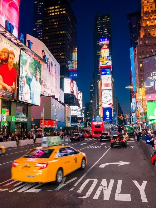 Times Square à la nuit tombée, écrans lumineux et taxi jaune sur la chaussée.